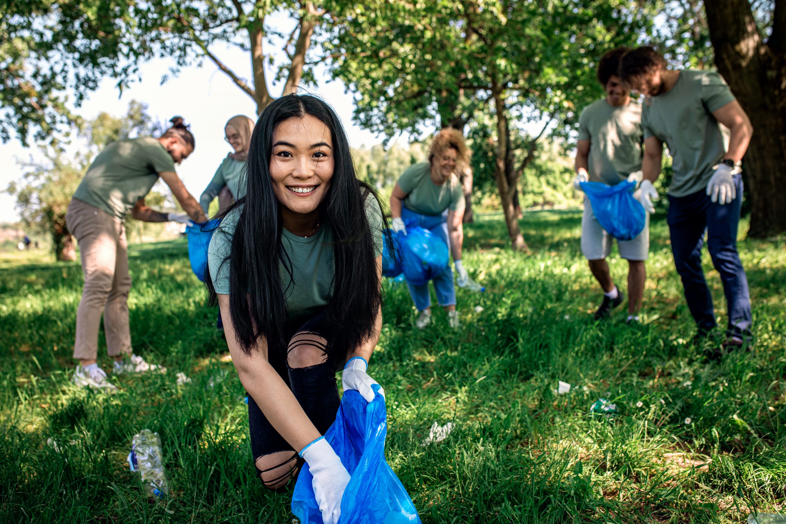 Portrait of young woman with garbage bags cleaning city park with friends